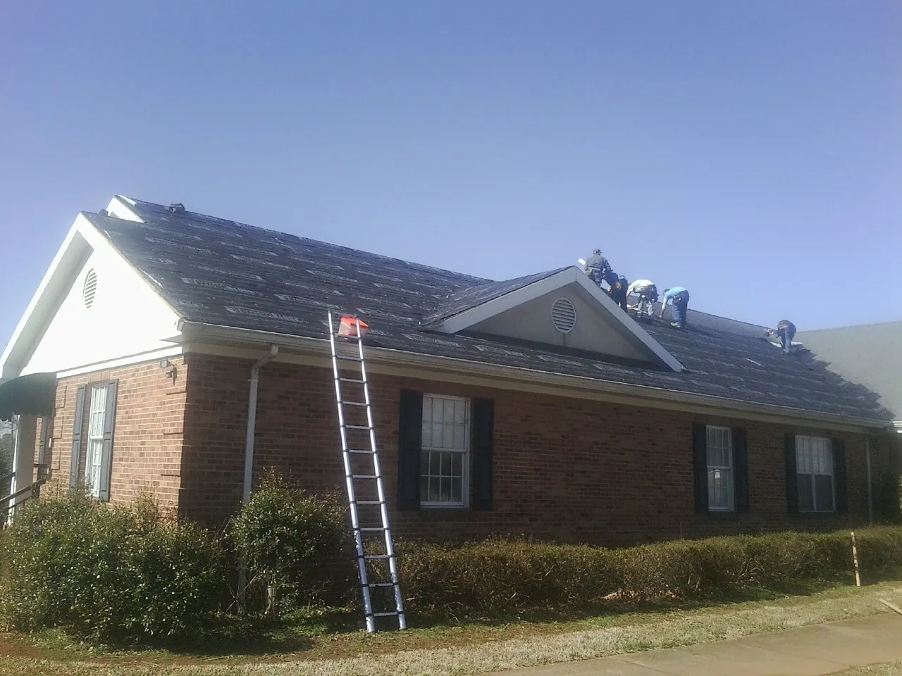 Crew tearing shingles off a brick ranch roof with a ladder set — Emergency Roof Repair work by our crew in Clare