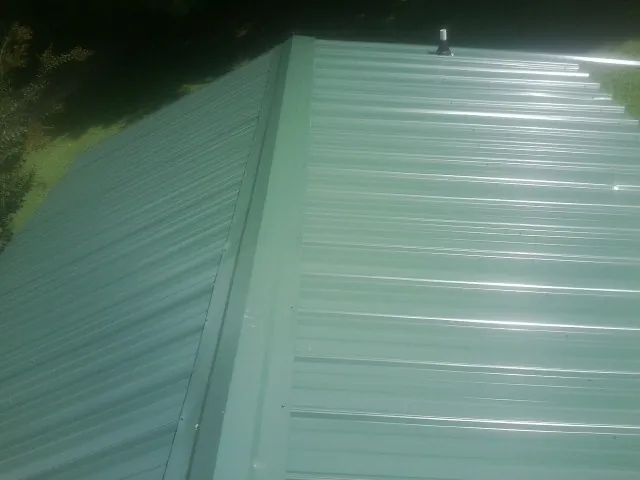 New green metal panels meeting at the ridge of a roof — Flat Roof Repair work by our crew in Clare