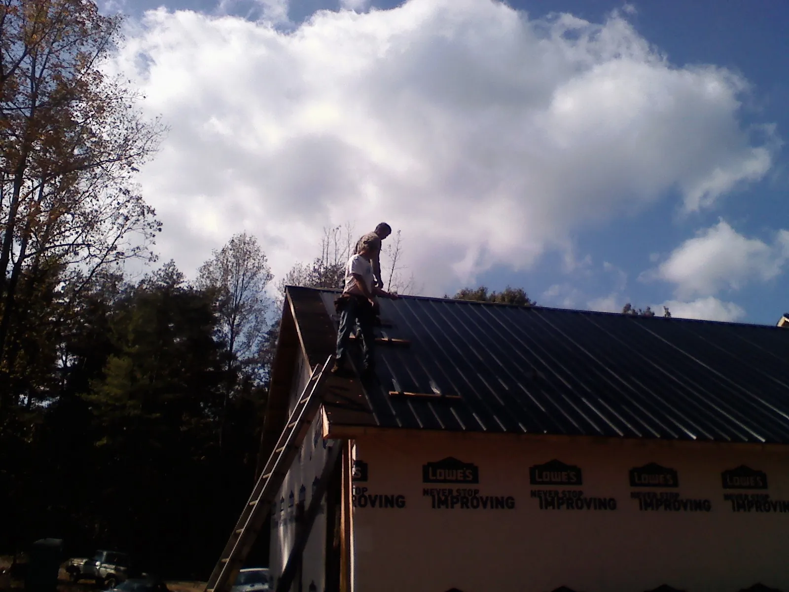Roofer fastening dark metal panels high against a cloudy sky, from a Roof Inspection job in Clare